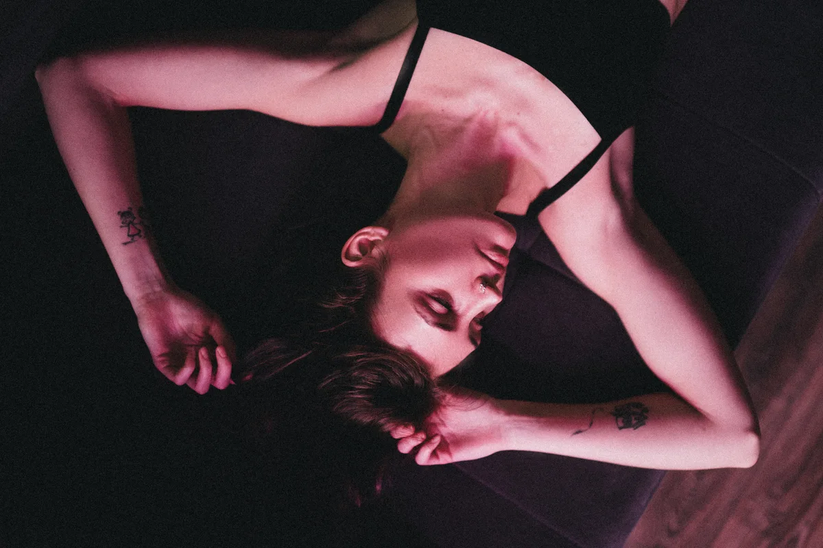 A reclining woman in a black dress under pink light.