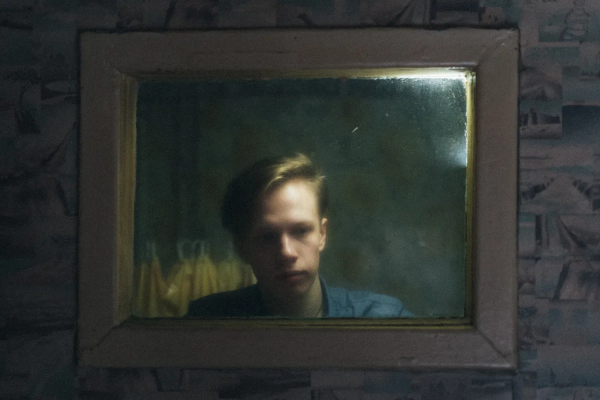 A man's face reflected in a weathered rectangular mirror.