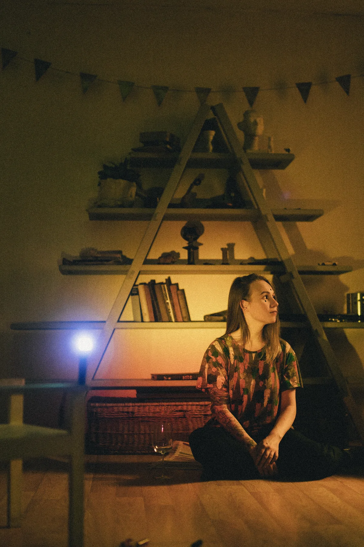 A woman seated beneath a triangular arrangement of shelves.