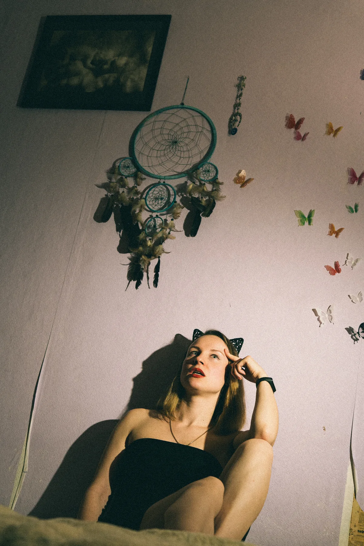 A woman reclining beneath hanging decorations on a pale wall.