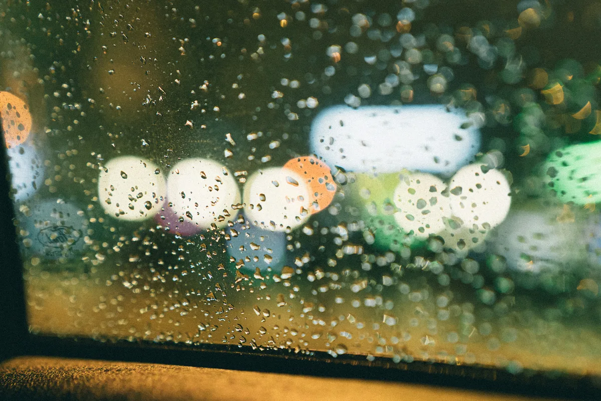 Water droplets on glass with out-of-focus white and green lights behind.