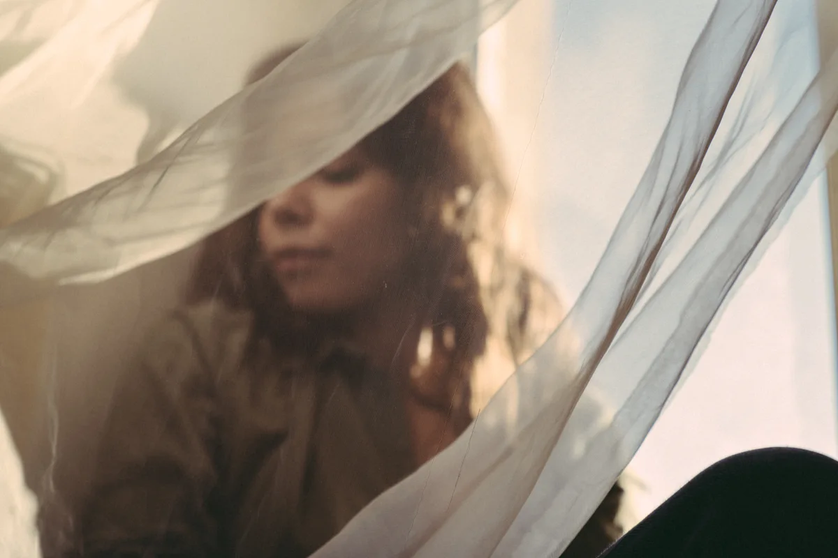 A woman's face partly obscured by translucent pale fabric.