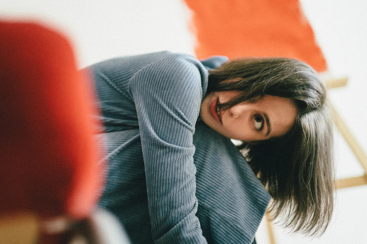 A woman in a grey sweater leaning against a red chair.