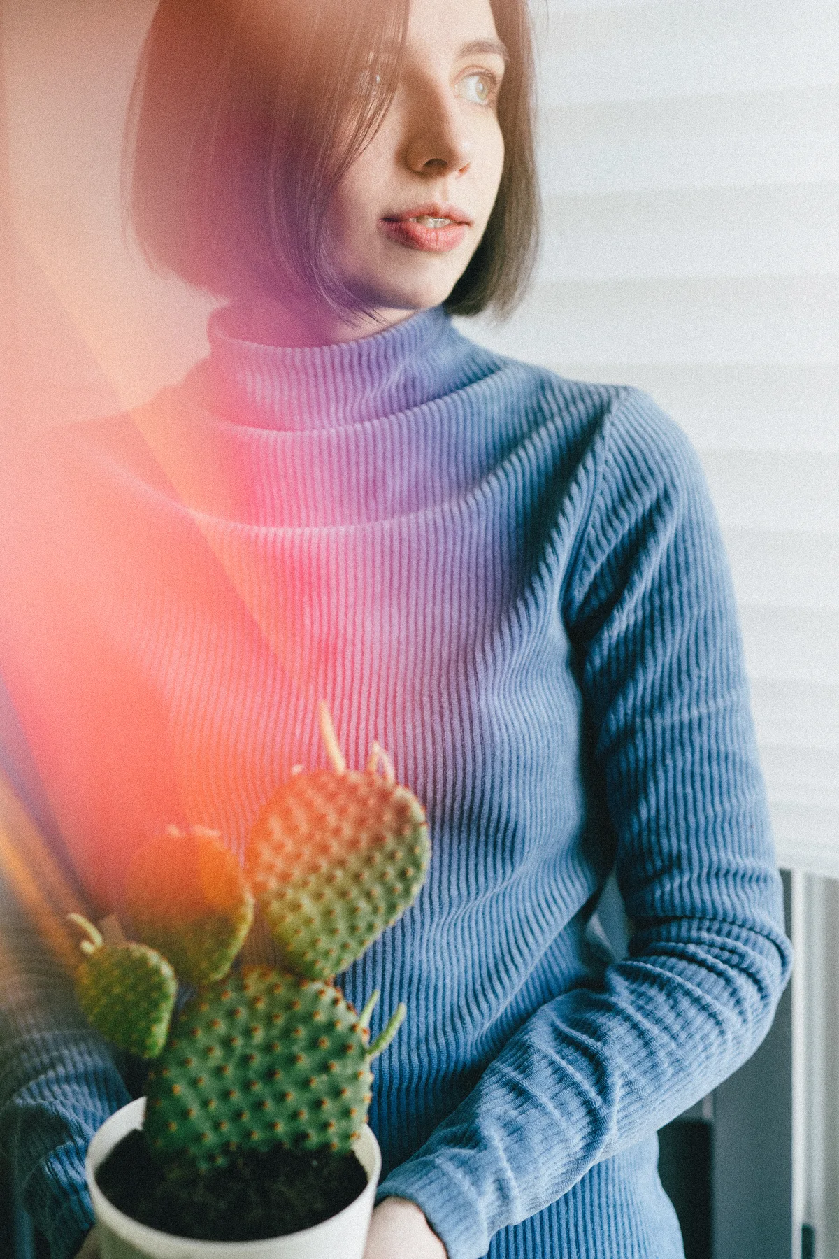 A woman in a blue sweater holding a small plant beside a window.