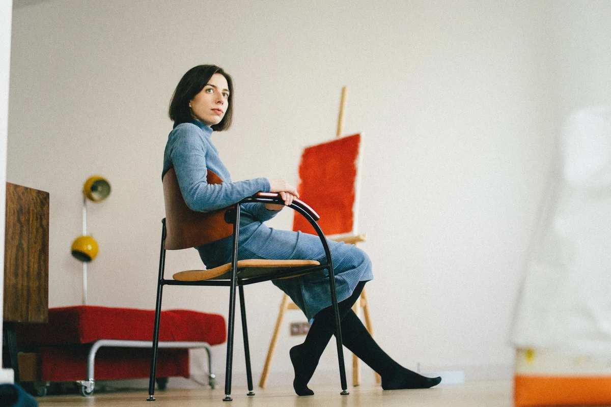 A woman seated on a red chair in a bright room.