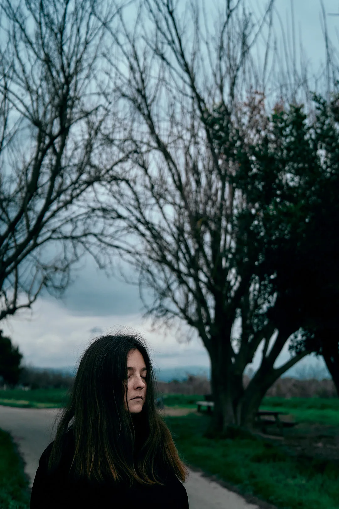 Portrait of a dark-haired woman with leafless trees behind her.