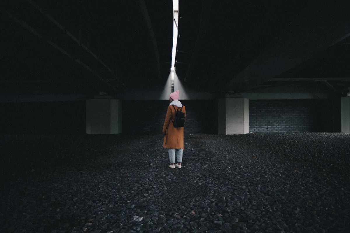 A person standing beneath a concrete structure under a narrow strip of daylight.