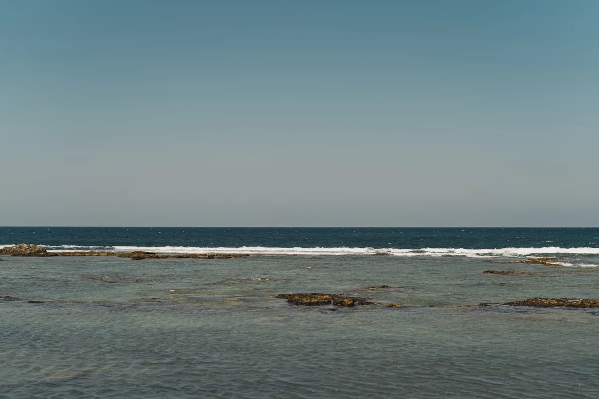 Low waves and rocks beneath a clear blue sea horizon.