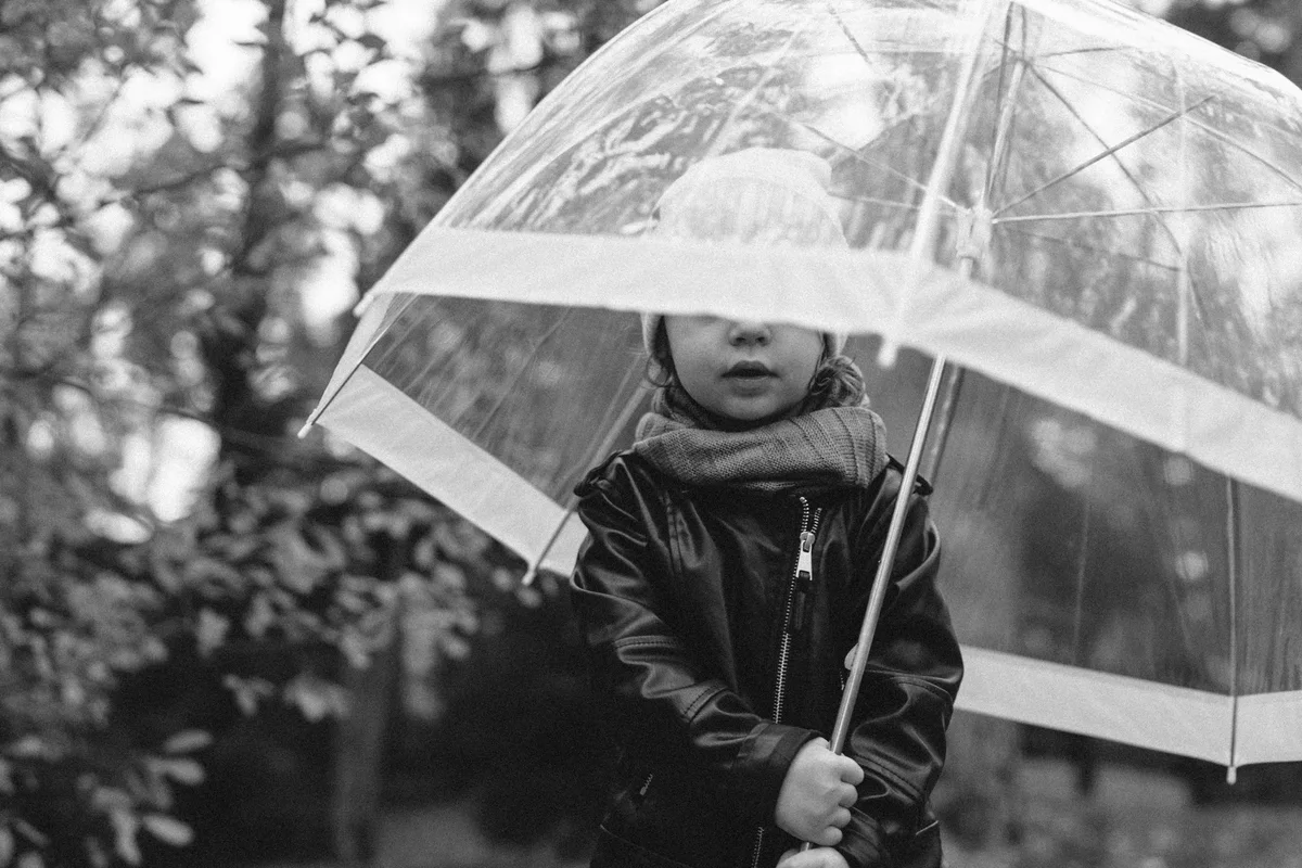 Black-and-white photograph of a child beneath a transparent umbrella.