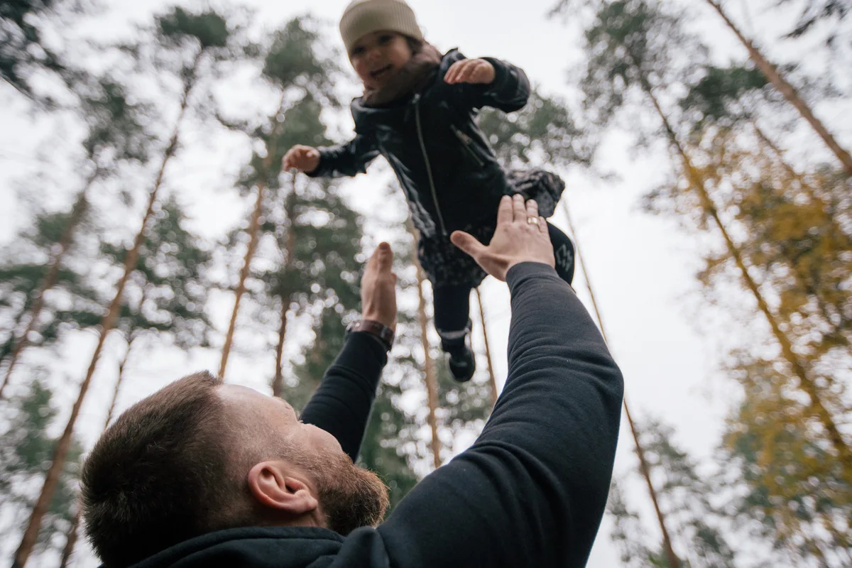An adult lifting a smiling child towards the trees.