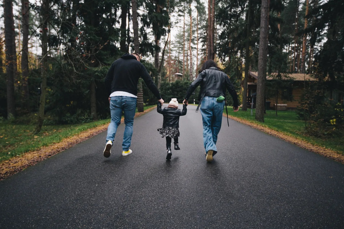 Two adults and a child moving away along a tree-lined road.