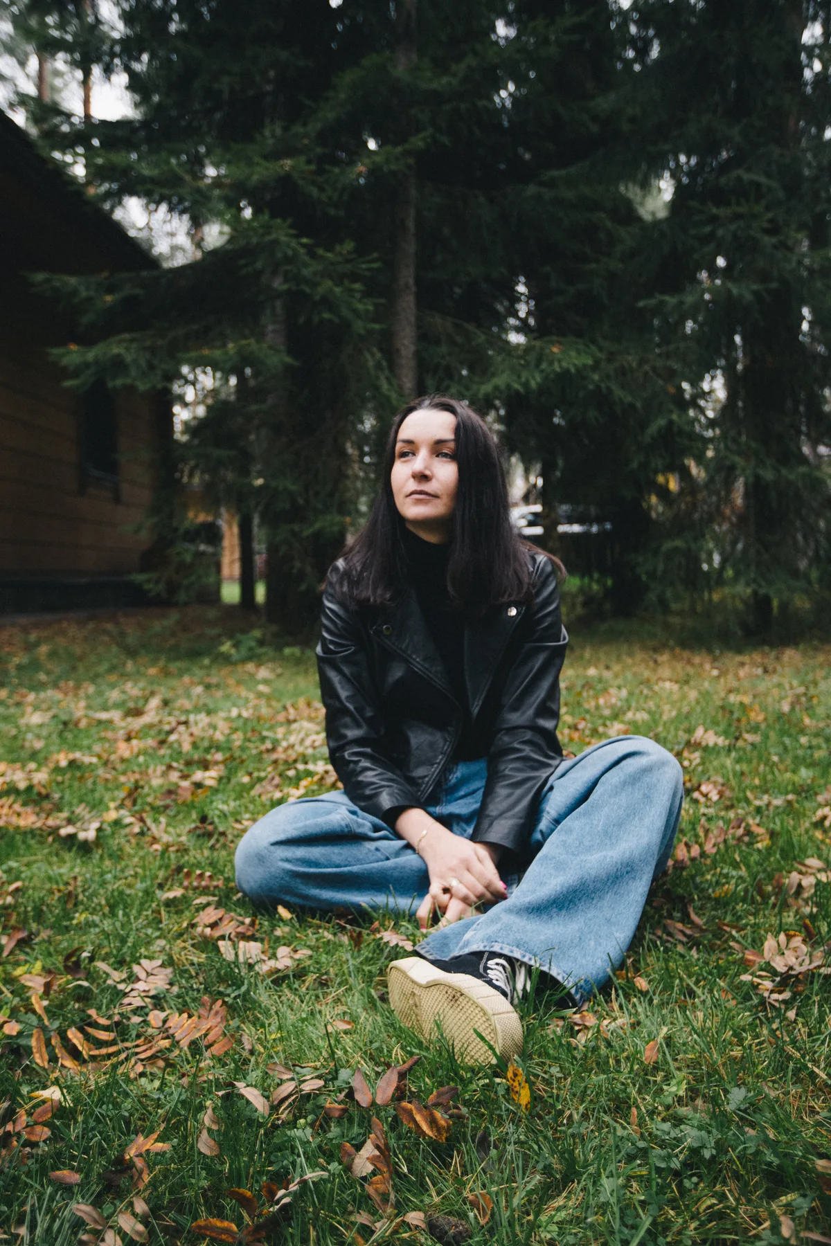A woman seated on the ground among grass and trees.