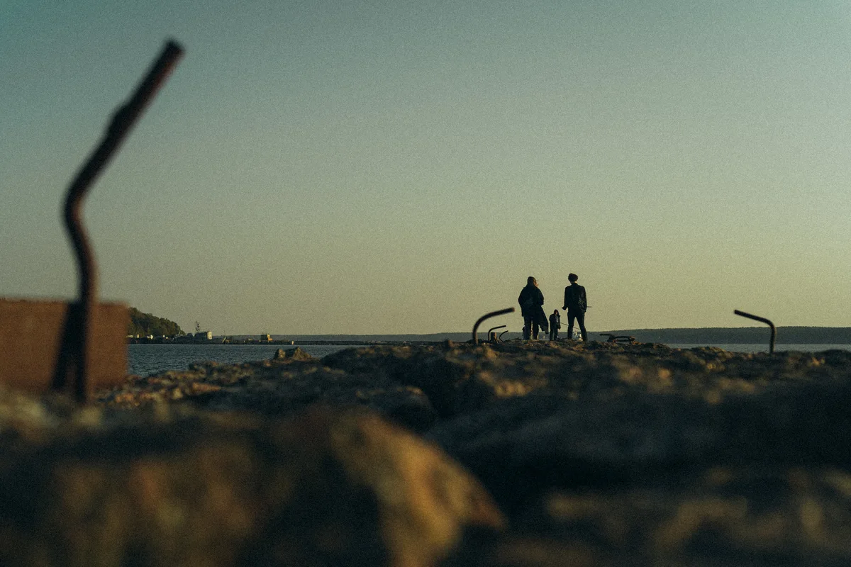 Two distant figures standing near the water behind foreground branches.
