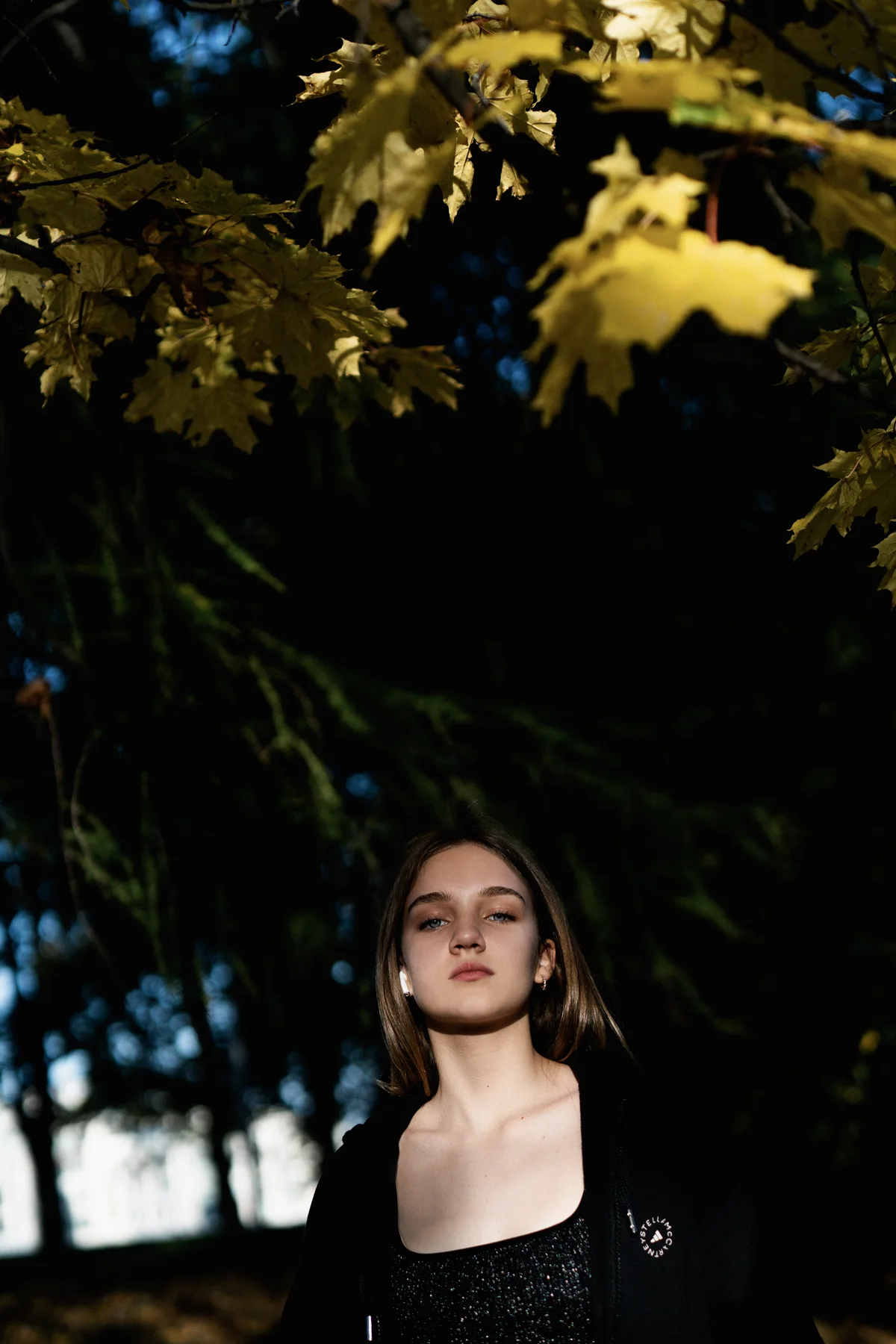 A woman standing below yellow leaves against dark trees.