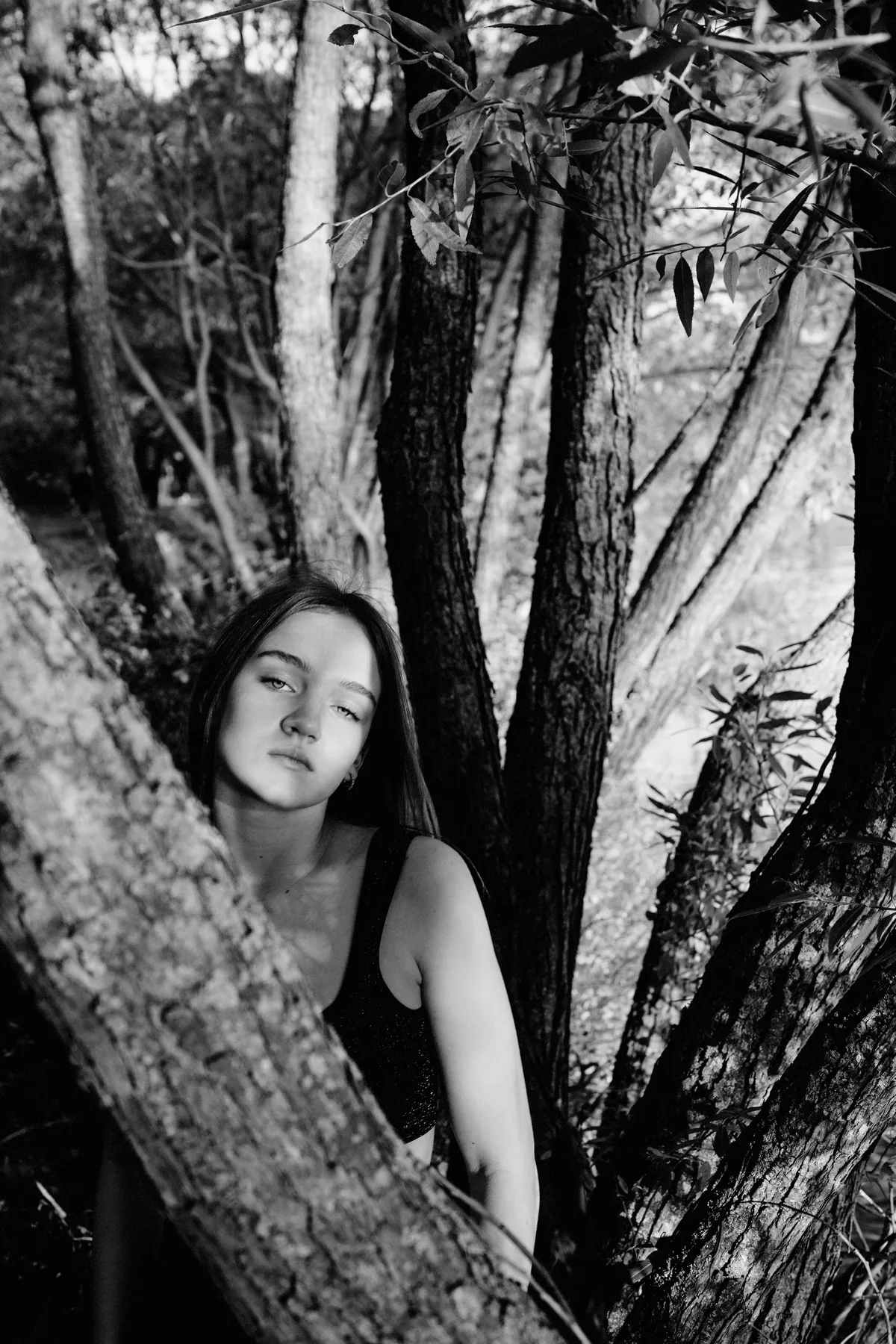 Black-and-white portrait of a woman beside a branching tree trunk.