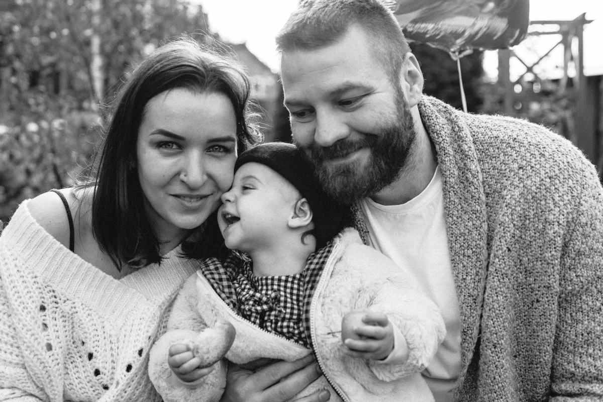 Black-and-white close photograph of two adults and a child kissing one of them.