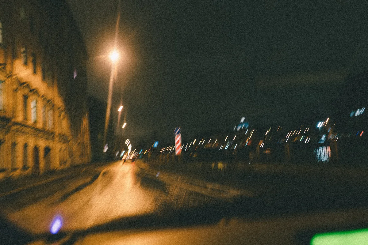 Blurred street lights and buildings seen from a moving vehicle at night.