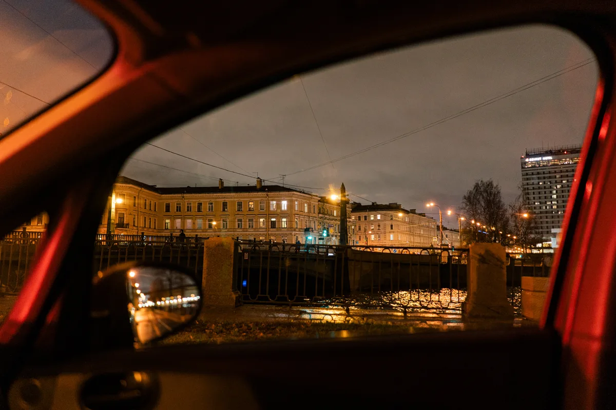 An illuminated building and water seen through a car's side window at night.