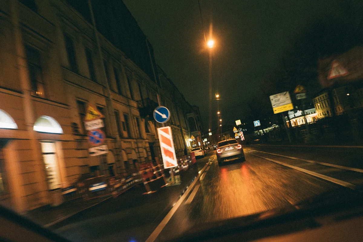 A night road with a vehicle ahead and blurred building lights.