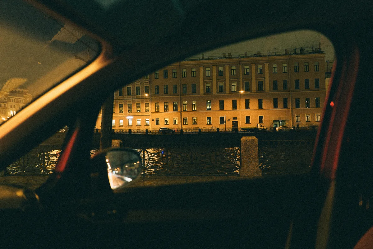 A lit building beyond a car window and wing mirror at night.
