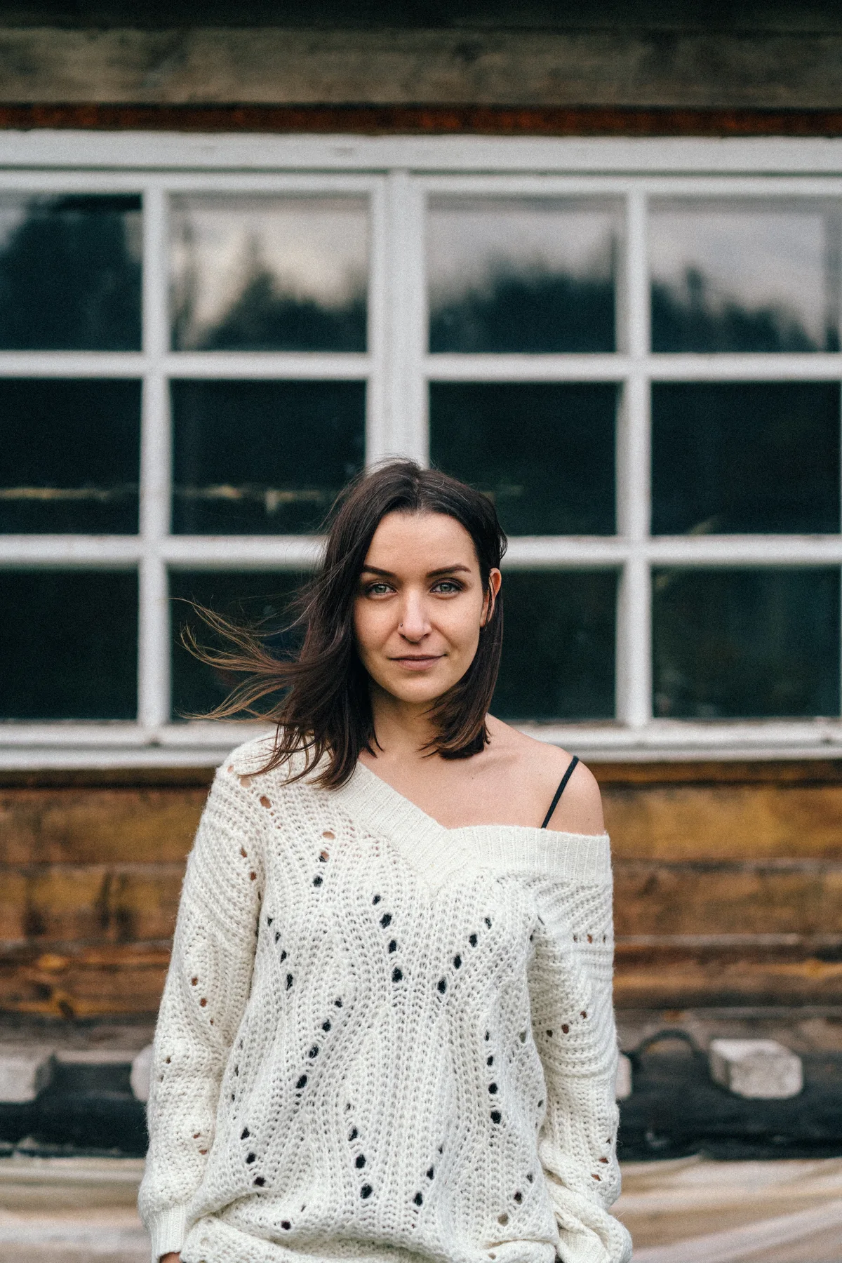 A woman in a pale sweater seated in front of a wooden building.