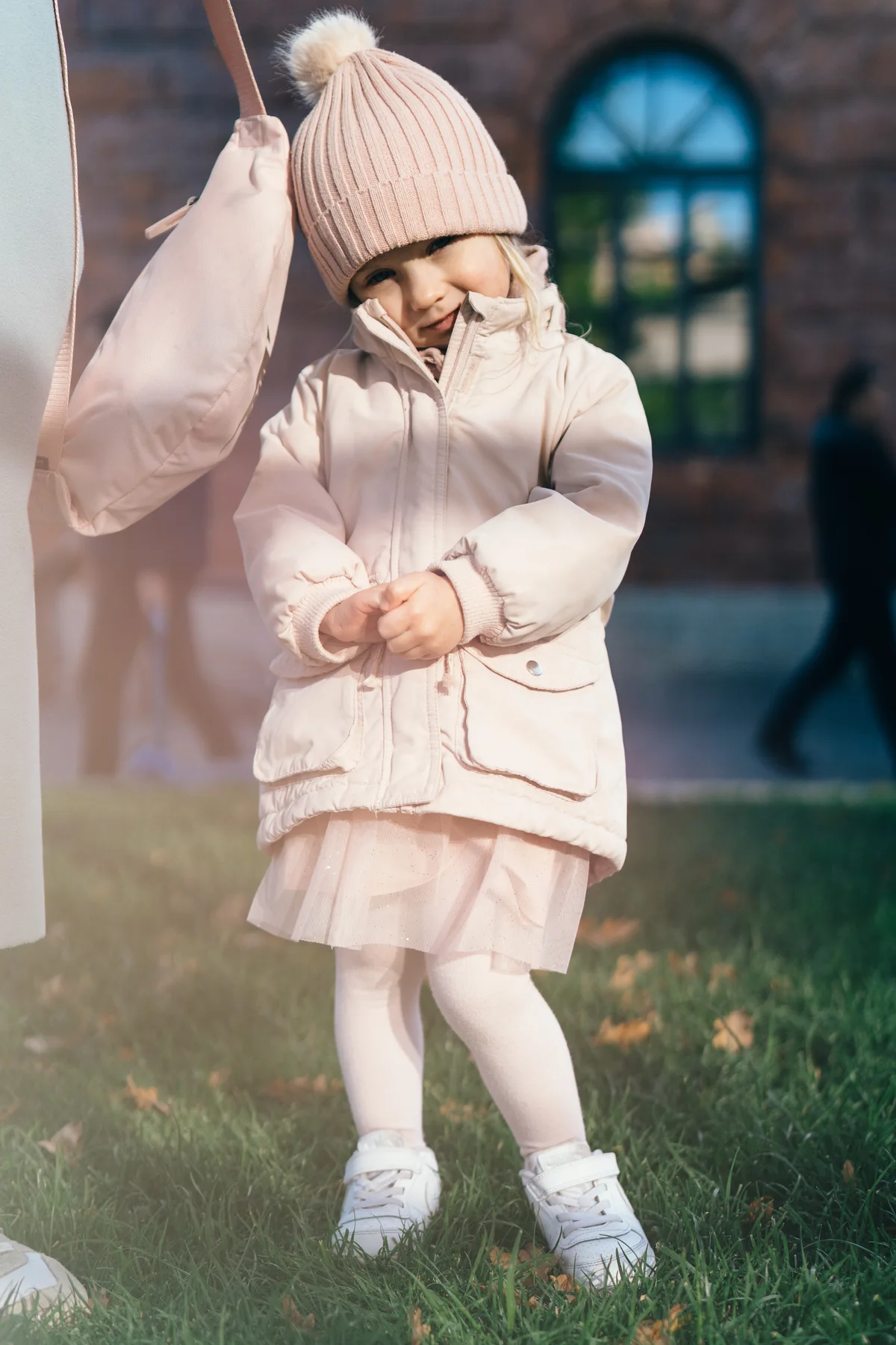 A child in pale pink clothes and a knitted hat outdoors.
