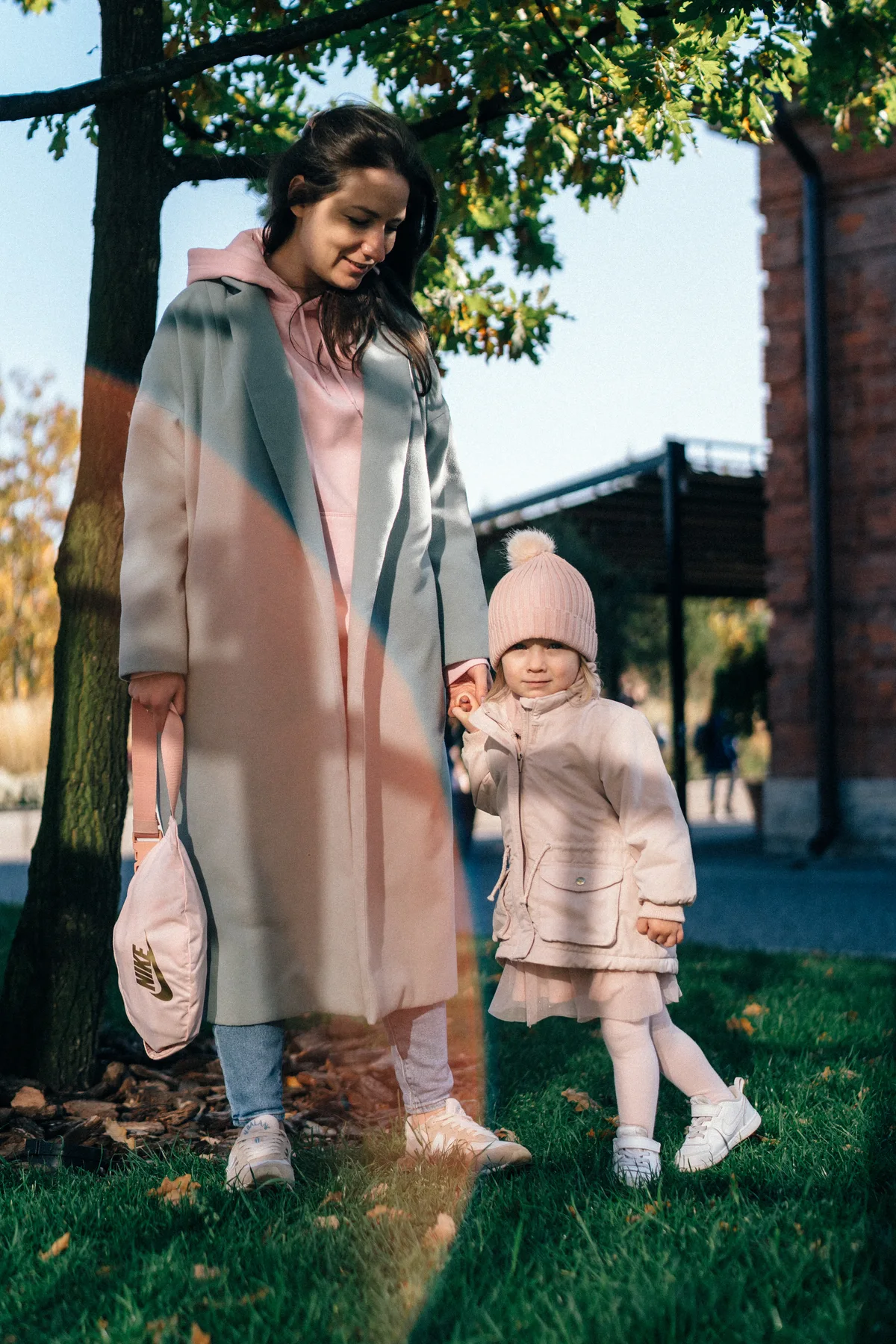 An adult and child standing together outdoors beneath a tree.