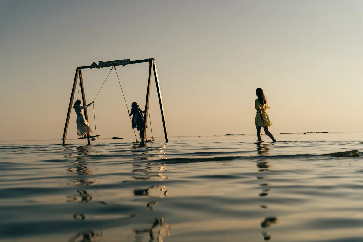 People playing on swings in shallow water in warm evening light.
