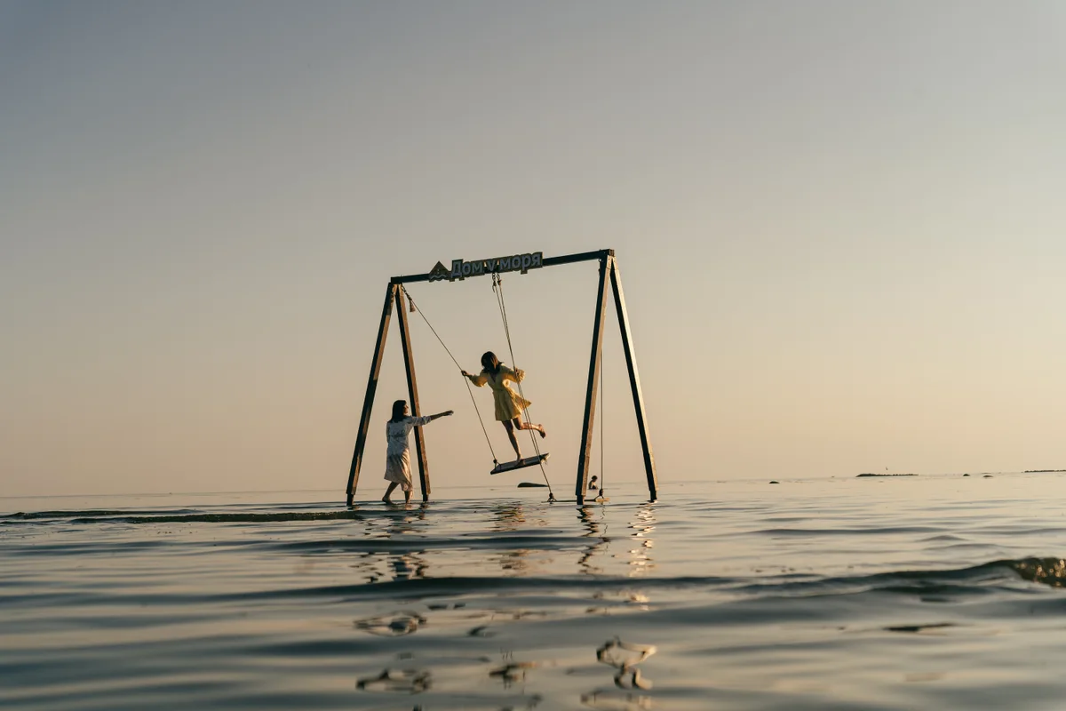 A person leaning outward from a swing over shallow water.