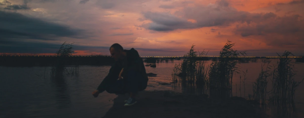 A figure by the water beneath an orange evening sky