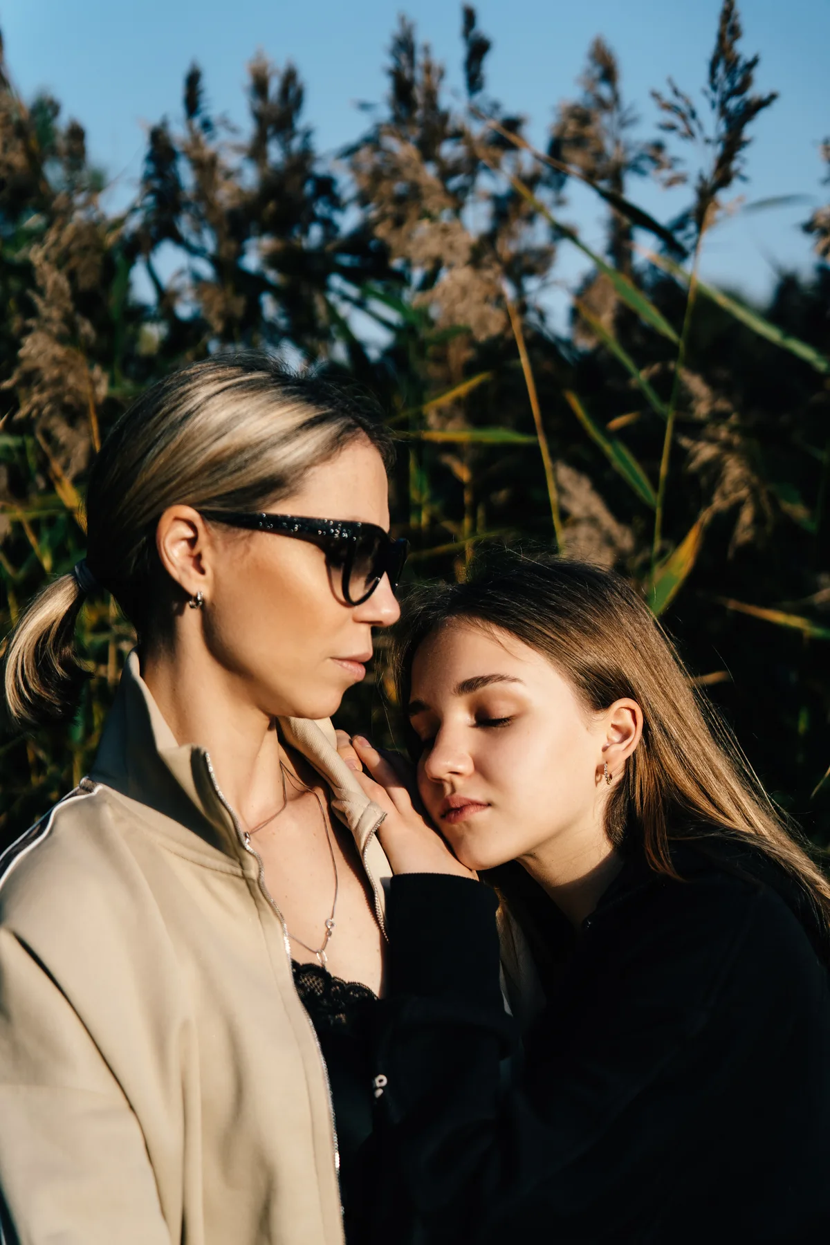 Two women close together in sunlight, one wearing sunglasses.