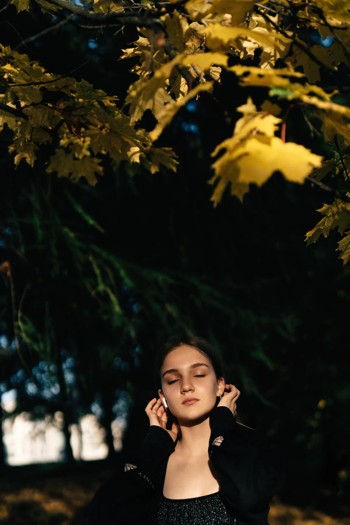 A woman with closed eyes below a canopy of yellow leaves.