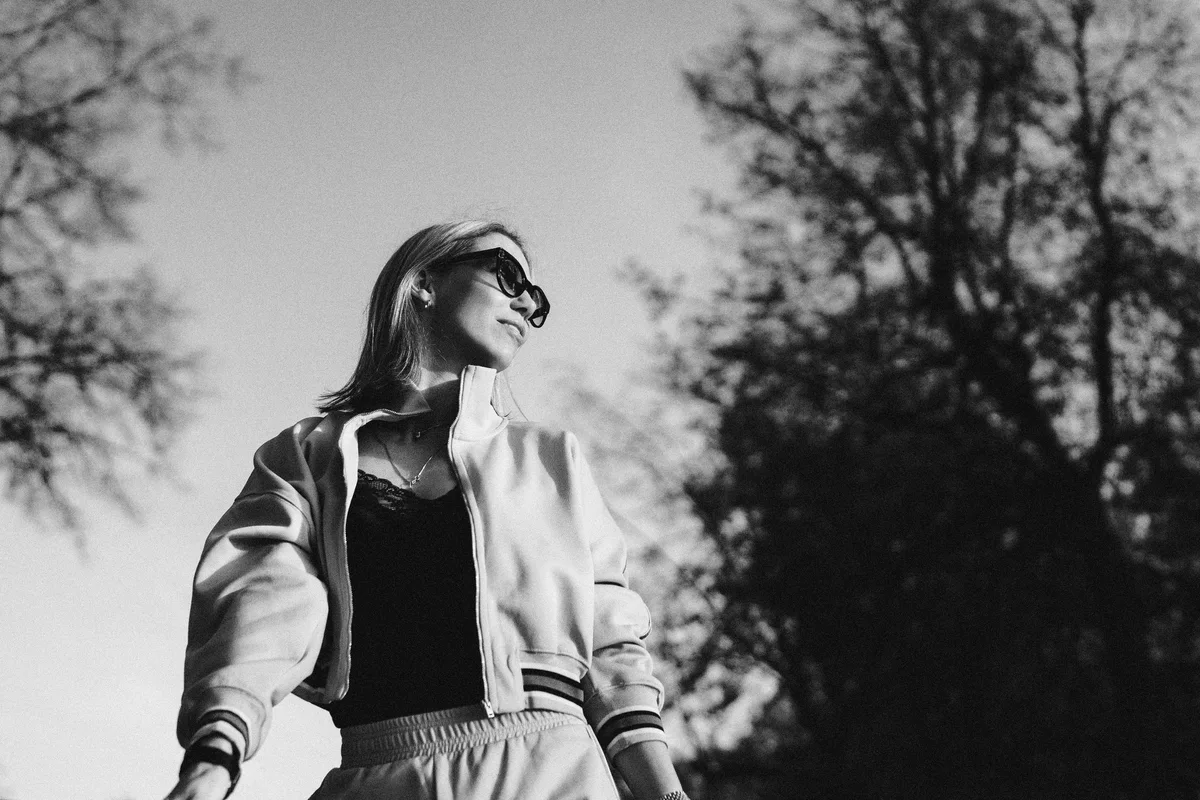 Black-and-white low-angle portrait of a woman wearing sunglasses outdoors.