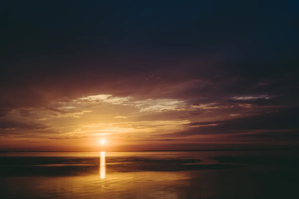 A low sun reflected vertically on the sea beneath dark clouds.