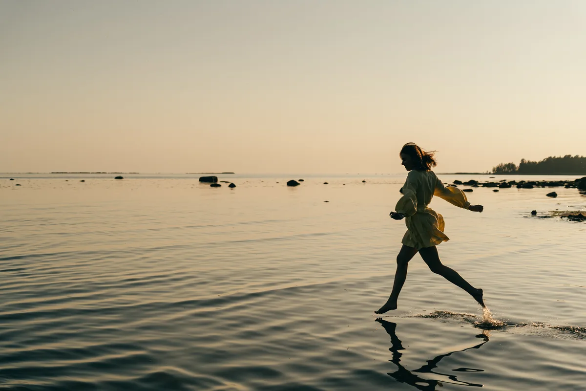 A child running through shallow water with a reflection beneath.