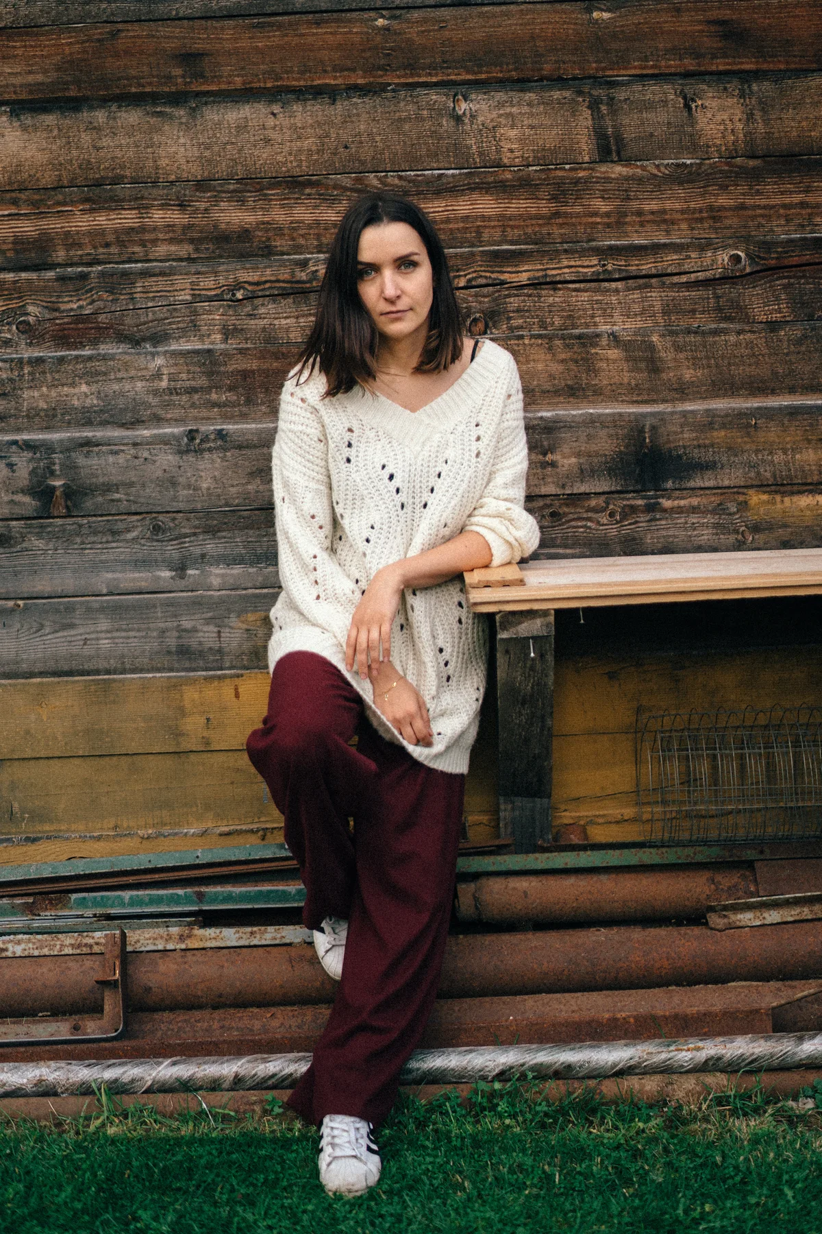 A woman leaning against a wooden wall beside a bench.